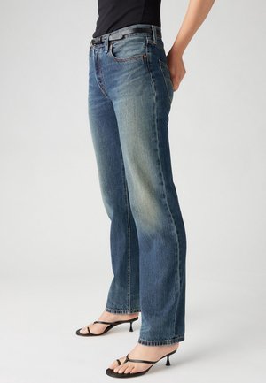 Hellblaue Jeans aus Denim mit geradem Bein, subtilen Verblassungen, fünf Taschen und einem Bund, der mit einem schwarzen Gürtel abgeschlossen ist.