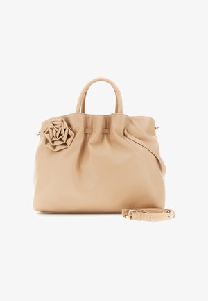 Beige læderhåndtaske med runde håndtag, en blomsterudsmykning på venstre side og en aftagelig skulderrem placeret foran.