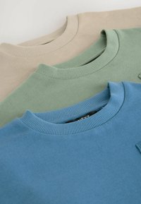 Drie crewneck sweatshirts in beige, groen en blauw. Elk heeft ribgebreide kragen en is gemaakt van zacht katoen met een soepele textuur.