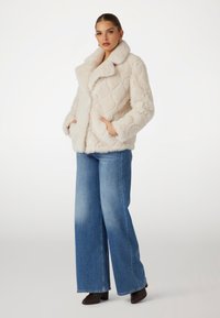 Puslinis dirbtinio kailio švarkas su tekstūruotu deimantiniu raštu, dideliu apykakle ir šoninėmis kišenėmis, derinamas su plačiomis mėlynomis džinsomis ir rudomis aukštakulnėmis.