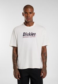 Bílý bavlněný tričko s textem "Dickies" v tučném tmavě modrém písmu a "DURABLE CLOTHES" červeně. Krátké rukávy a volný střih.