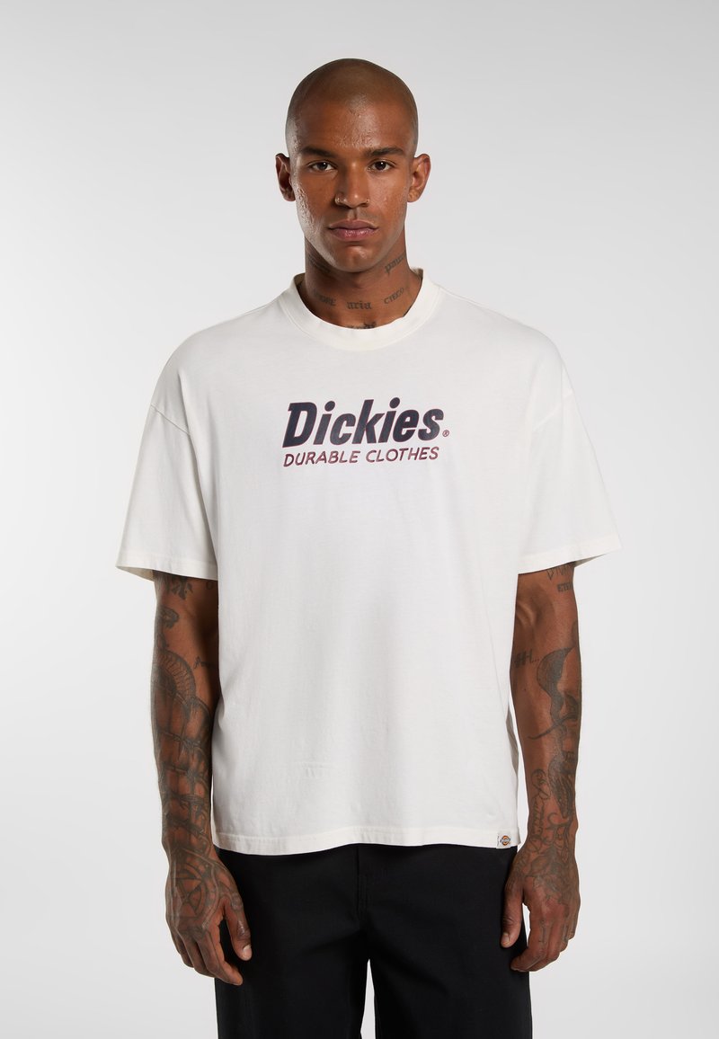 Bílý bavlněný tričko s textem "Dickies" v tučném tmavě modrém písmu a "DURABLE CLOTHES" červeně. Krátké rukávy a volný střih.