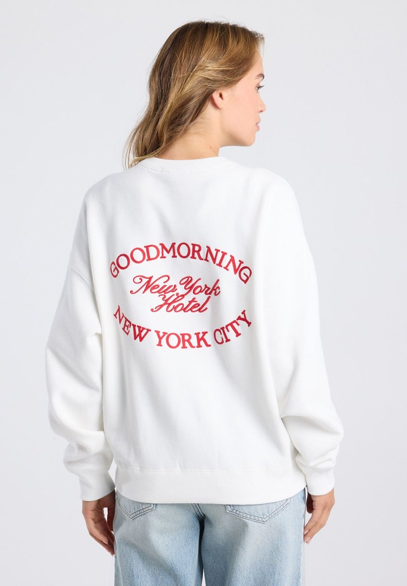 Weißer Sweatshirt mit rotem gesticktem Text "GOODMORNING NEW YORK HOTEL NEW YORK CITY" auf der Rückseite. Legere Passform, lange Ärmel.