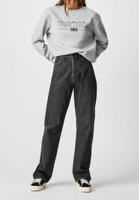 Sudadera gris con el logo "PEPE JEANS", combinada con vaqueros de mezclilla oscuros y holgados, y zapatillas negras con suelas blancas.