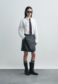 Λευκό πουκάμισο με κουμπιά, σκούρα γραβάτα, μαύρη δερμάτινη μίνι φούστα, μαύρες μπότες μέχρι το γόνατο με λεπτομέρεια αλυσίδας, γκρι κάλτσες μέχρι το γόνατο, κομψό χτένισμα.