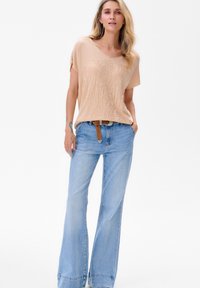 Lichtbeige kortom mouwtop met een gestructureerd patroon, gecombineerd met lichtblauwe flared jeans en een bruine riem met een metalen gesp.