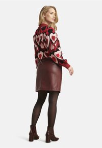 Red and black heart-patterned sweater paired with a brown faux leather skirt. Model wears black tights and burgundy heeled ankle boots.