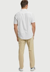 Witte short-sleeve shirt van lichtgewicht stof, met achterkant plooi detail, beige broek en witte sneakers met gekleurde accenten.