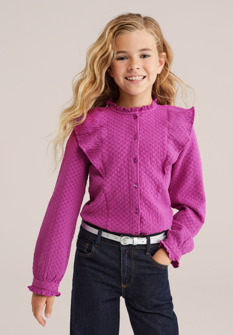 Fuksijaste srajce z gumbi, z teksturirano tkanino, nabranimi rameni in dolgimi rokavi. Ujemajo se s temnimi kavbojkami in belim pasom.