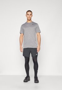 Sportliches Herrenoutfit bestehend aus einem kurzärmligen, heather-grauen Shirt, schwarzen Shorts und schwarzen Kompressionsleggins mit Nike-Logo.