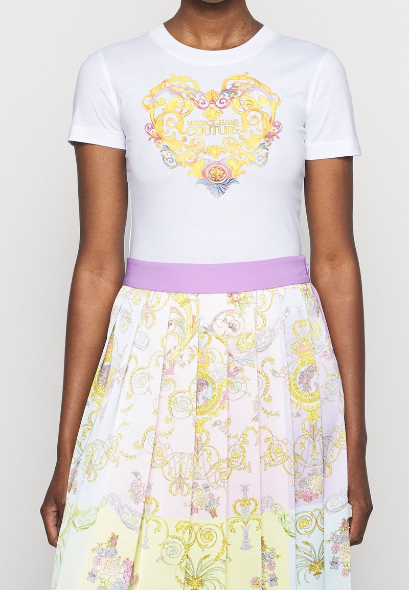 Biała bawełniana koszulka z ozdobnym żółto-niebieskim motywem serca, w połączeniu z plisowaną spódnicą w pastelowych kolorach i kwiatowymi wzorami.