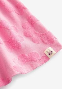 Tissu rose avec des motifs floraux en relief et une petite étiquette cousue représentant un visage de lapin avec des joues roses.