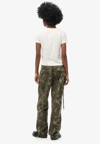Witte katoenen T-shirt gecombineerd met groene camouflage cargo broek met zijzakken en drawstring onderranden, gedragen met zwarte schoenen.