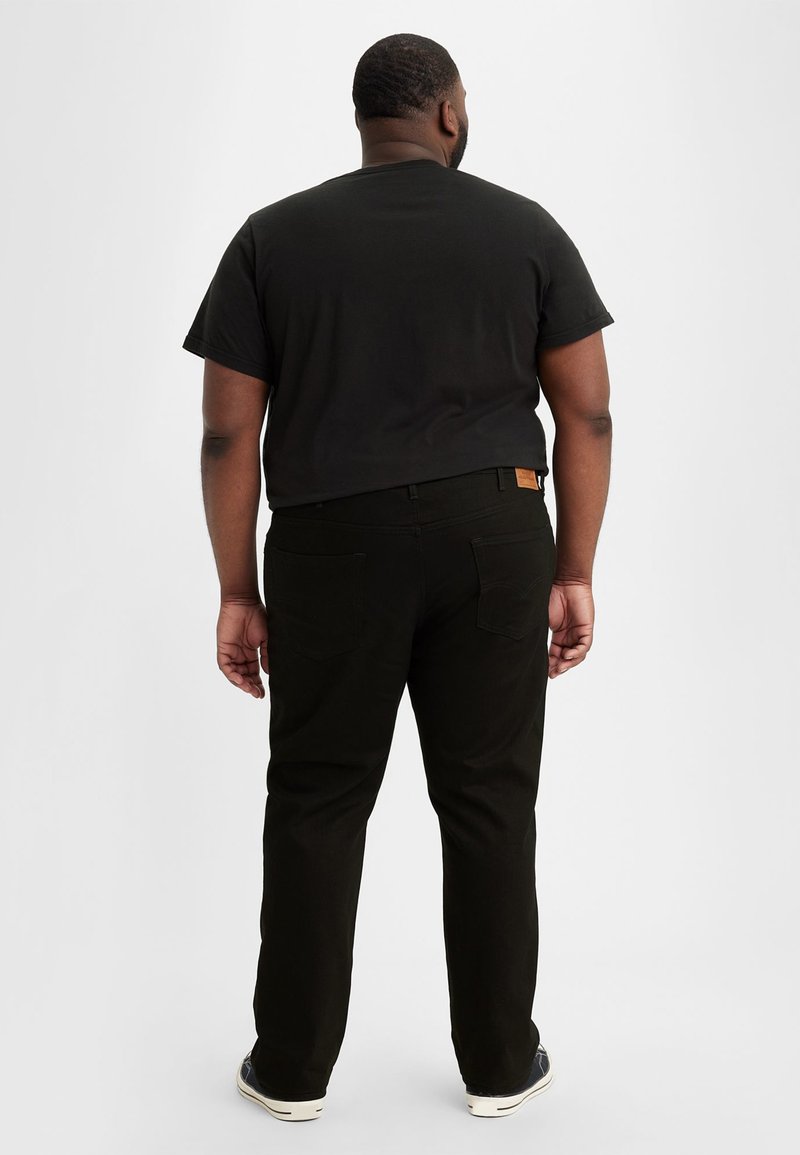 T-shirt noir à manches courtes accompagné de pantalons vert foncé. Le t-shirt a une coupe classique, et les pantalons possèdent une patch en cuir et des poches.