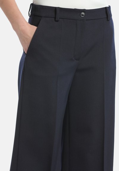 Marineblauwe broek met een getailleerde pasvorm, voorzien van een platte voorkant, zijzakken en een enkele knoopsluiting. Gemaakt van een gladde, lichte stof.