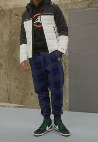 Dunjacka i svart och vitt med röda detaljer, svart huvtröja under, rutiga mjukisbyxor i blått och grönt, gröna och svarta höga sneakers.