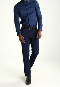 Marinblå skjorta med knappar och en mjuk textur, ihop med mörk marinblå byxor och svarta läderskor. Slim fit med en klassisk kragdesign.