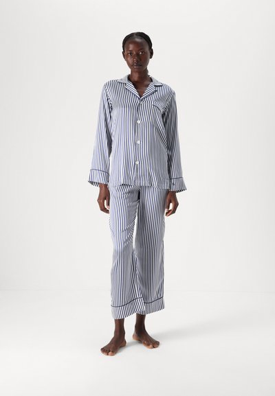 Ensemble de pyjama rayé bleu et blanc en tissu léger ; comprend une chemise à boutons avec col et un pantalon assorti avec des accents aux ourlets.