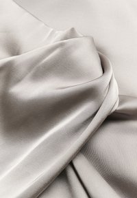 Tissu en satin gris pâle lisse et brillant avec des plis doux et un drapé délicat, mettant en valeur sa texture soyeuse et sa surface réfléchissante.