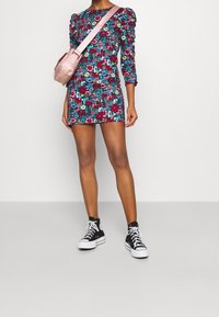 Robe mini à motif floral avec des manches longues et des épaules froncées. Portée avec des baskets montantes noires et un petit sac bandoulière rose.