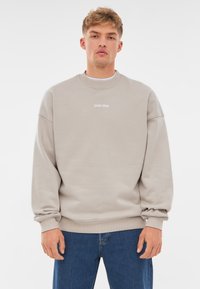 Sudadera gris claro con cuello redondo, hombros caídos y puños acanalados. Presenta un sutil logo "JOHNNY URBAN" en blanco en la parte frontal.