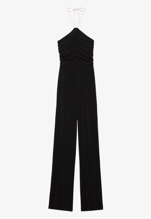 Černý overal na ramínka s nařasenými detaily na těle, širokými nohavicemi a nastavovacími tkaničkami. Vyrobeno z měkké a pružné látky.