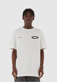 Hvid bomulds t-shirt med et sort torn cirkel grafik på brystet og brandlogo. Løs pasform, korte ærmer og rund hals design.