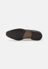 Semelle de chaussure avec une finition en caoutchouc noir texturé, présentant une section en cuir marron, un accent circulaire et un motif géométrique pour l'adhérence.