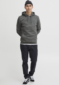 Gray hoodie with kangaroo pocket and drawstring hood, paired with black pants. Worn with black sneakers and a dark knit beanie.