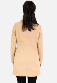 Abrigo de lana beige con un acabado texturizado, forma ajustada y mangas largas, cuenta con una costura trasera recta y una longitud a mitad del muslo.