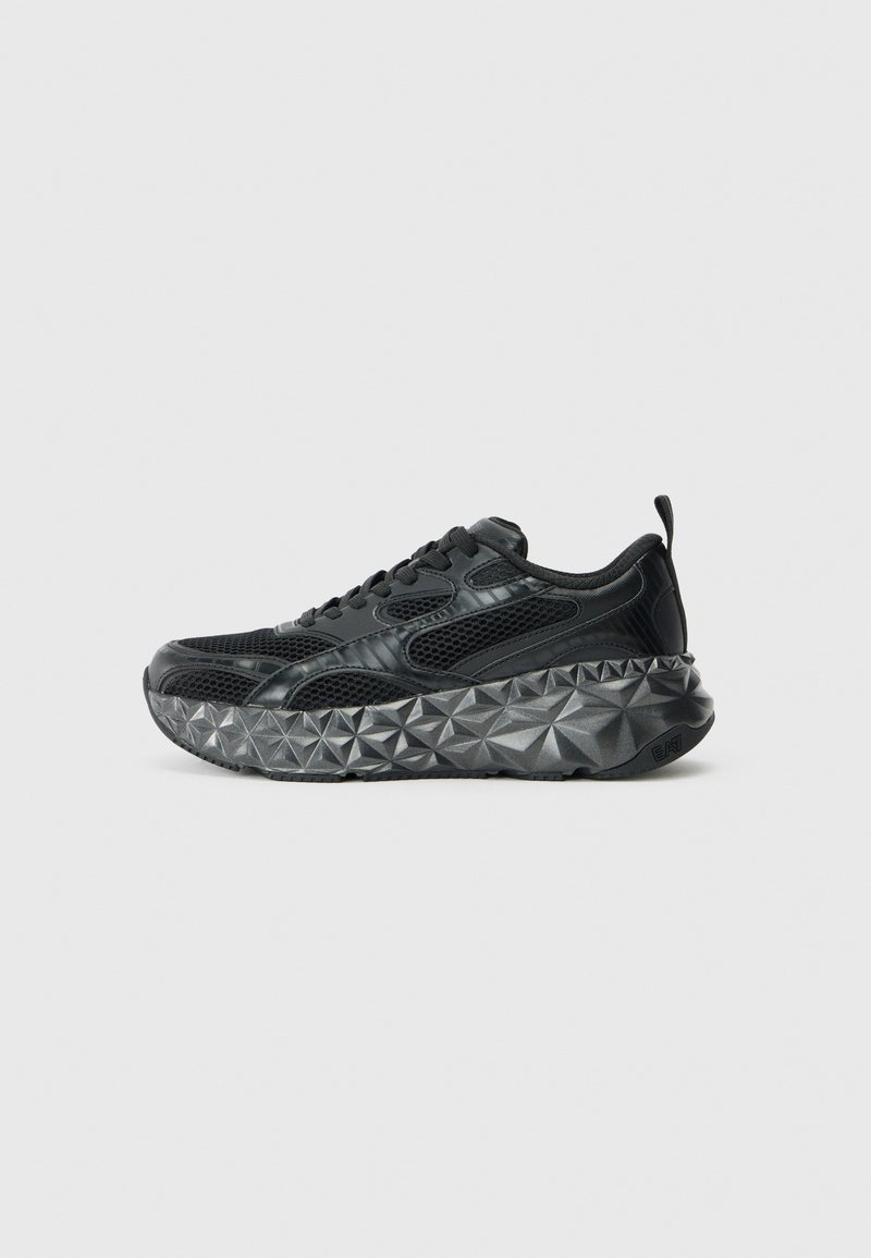 Schwarze Sneaker mit einem strukturierten Mesh-Obermaterial und synthetischen Akzenten, ausgestattet mit einer auffälligen Sohle mit geometrischem Muster. Der Schnürdesign umfasst eine Zuglasche.