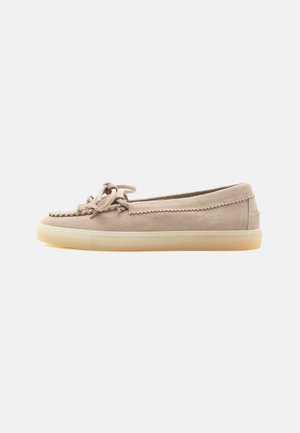 Chaussure style mocassin en daim beige avec nœud de lacets sur le dessus et semelle en caoutchouc claire, affichée de profil sur fond blanc.
