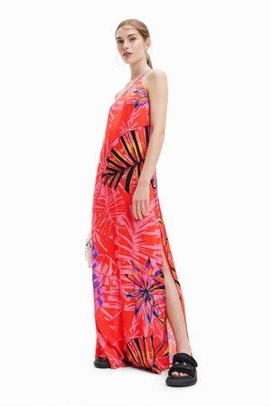 Abito maxi rosso con un motivo di foglie tropicali in rosa, nero e blu. Ha una scollatura all'americana e fessure laterali. Indossato con sandali neri.