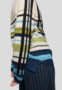 Gestrickter Pullover mit cremefarbenem Grundton, versehen mit mehrfarbigen Streifen in Blau, Grün und Schwarz. Auffällige breite Bündchen und ein wellenförmiger Saum.