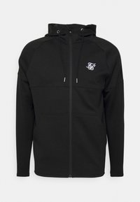 Musta vetoketjullinen huppari, jossa on säädettävä huppu, raglanhihoja, etutaskut ja valkoinen brodeerattu logo. Valmistettu pehmeästä ja joustavasta kankaasta.