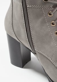 Bottine en daim gris avec talon bloc, fermeture éclair latérale et devant à lacets avec œillets métalliques sur fond blanc.