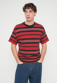 Κόκκινο και μαύρο ριγέ t-shirt με γκρι λεπτομέρειες, κοντά μανίκια και στρογγυλή λαιμόκοψη. Το ύφασμα φαίνεται υφασμένο με ελαφρώς ριγέ υφή.