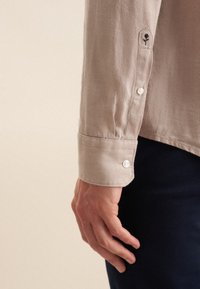 Lichtbeige linnen shirt met mouwen, voorzien van parelknopen, een ronde manchette en subtiele bloemenborduursels op de manchette.