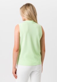 Mouwloze mintgroene polo, gladde stof, relaxte fit, klassieke kraag, met subtiele stiksels en een eenvoudige stijl, gedragen met witte broeken.