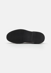Suola di scarpa nera con un motivo di presa texture e superficie liscia, caratterizzata da un tacco pronunciato e un design della punta affusolata.