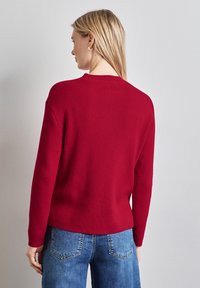 Maglione a coste rosso con maniche lunghe, scollatura a girocollo e vestibilità comoda. Abbinato a jeans in denim blu con un taglio classico.