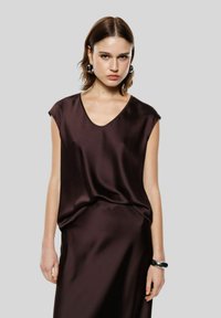 Top a maniche corte, scollo a V profondo in satin marrone scuro, caratterizzato da una vestibilità comoda e una texture liscia, abbinato a una gonna coordinata.