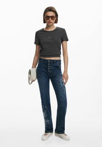 Dark gray cropped t-shirt, blue high-waisted jeans with embroidered details, and light footwear. Accessory: small white handbag.