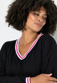Musta pitkähiha-paita V-kaula-aukkolla, jossa on vaaleanpunavalkoraidallinen kaulus. Pehmeä tekstuuri ja rento istuvuus.