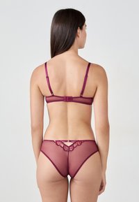 Set di lingerie malva realizzato in tessuto di rete trasparente, con dettagli in pizzo, spalline regolabili e una chiusura decorativa sulla schiena. Presenta un'applicazione di dettagli delicati.
