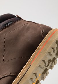 Ruskeat vedenpitävät saappaat, joissa on sileä nahkainen päällinen, erottuva oranssi tehoste pohjassa sekä kuvioitu kumipohja, jossa on kestävä uramalli.