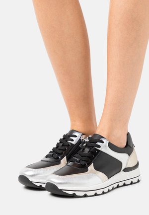 Zwart-zilveren sportschoenen met metallic accenten, een getextureerd oppervlak, zwarte veters en een witte rubberen zool met een zigzagpatroon.