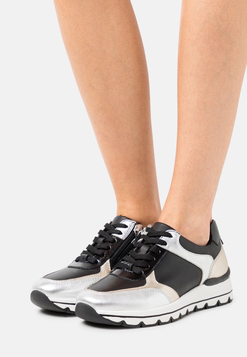 Scarpe da ginnastica nere e argento con accenti metallici, superficie testurizzata, lacci neri e suola in gomma bianca con motivo a zigzag.