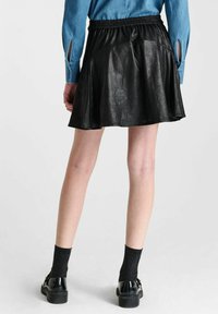 Zwarte faux leren rok met een uitlopende vorm en een elastische tailleband. Gecombineerd met glanzende zwarte schoenen en gestructureerde zwarte sokken.