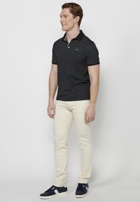 Czarny polo z subtelnym geometrycznym wzorem, z krótkim rękawem i czarnym kołnierzykiem. Noszony z kremowymi spodniami slim-fit i granatowymi sneakersami.